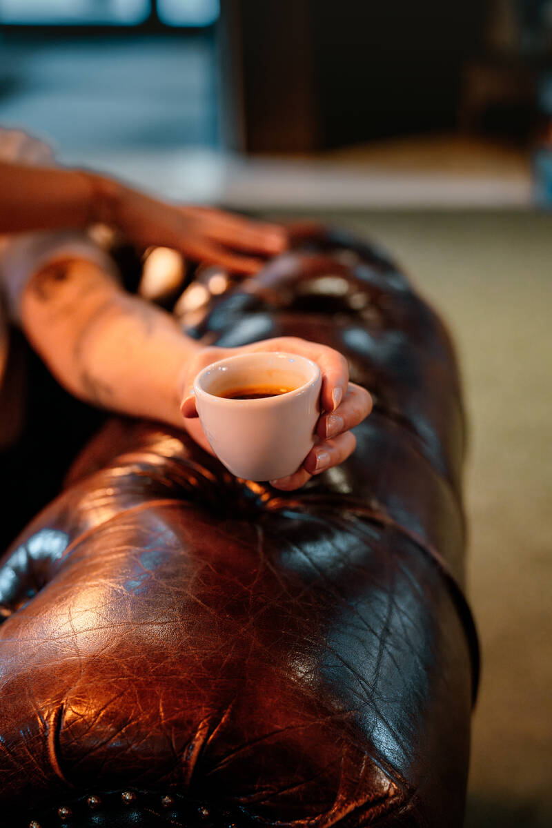 Eine Tasse Espresso die in der Hand gehalten wird, im Hintergrund ein Ledersofa.