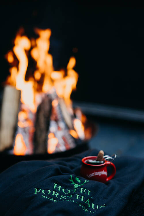 Glühwein auf einer Decke mit Hotellogo vor einer Feuerschale.