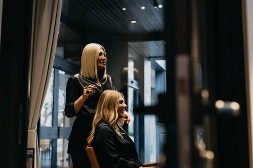 Eine blonde Friseurin macht einer Frau die Haare, die in einem Stuhl sitzt.