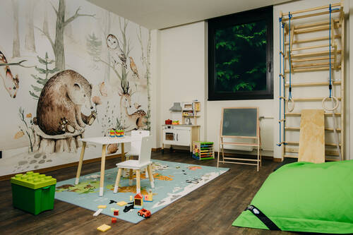 Spielzimmer mit bunter Tapete und verschiedenen Spielmöglichkeiten für Kinder.