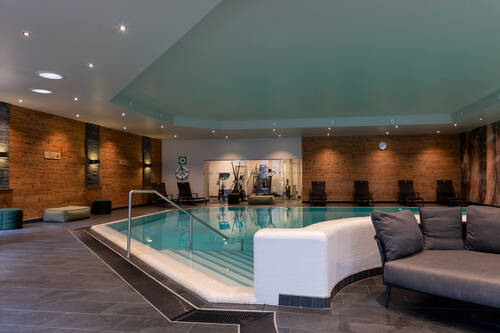 Indoor-Pool mit Loungemöbeln und Liegen.