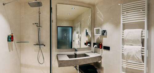 Badezimmer mit Waschbecken, Dusche und Heizkörper mit Handtüchern.