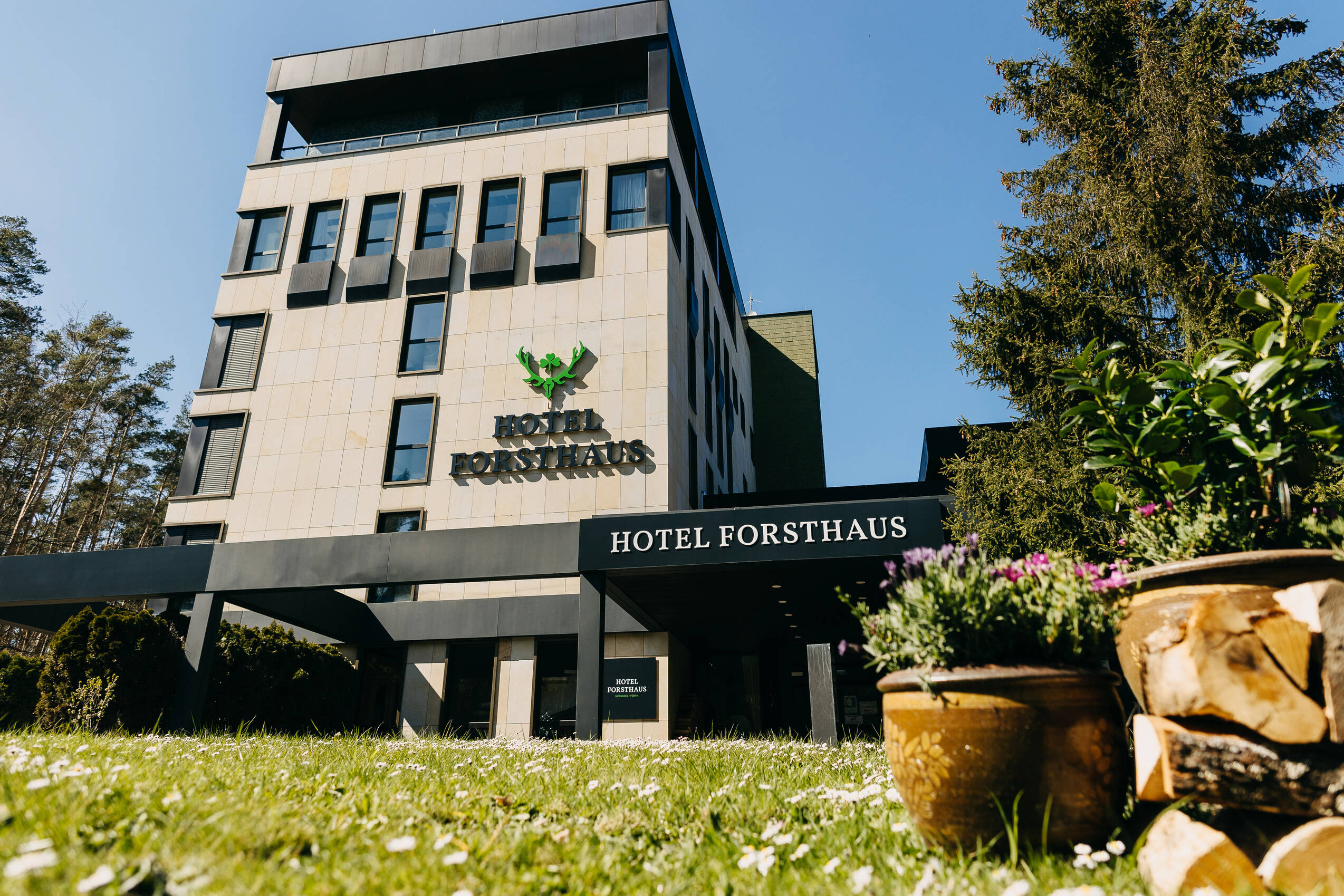 Außenansicht des Hotels mit Rasen, Blumen und Bäumen.