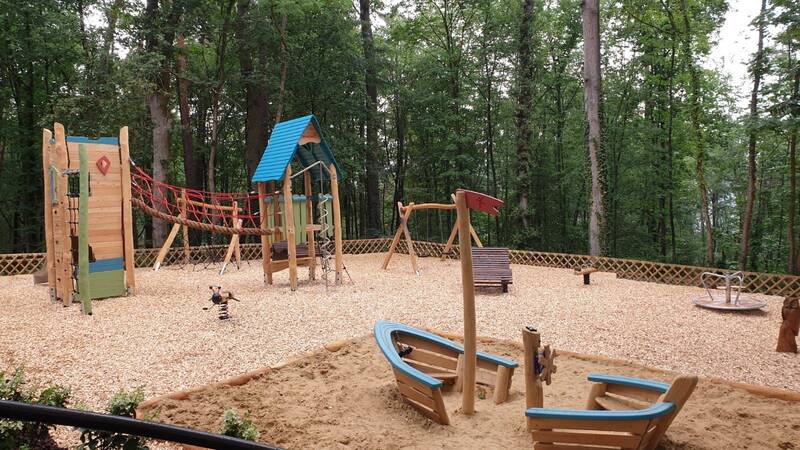 Spielplatz mit verschiedenen Geräten, im Hintergrund Wald.